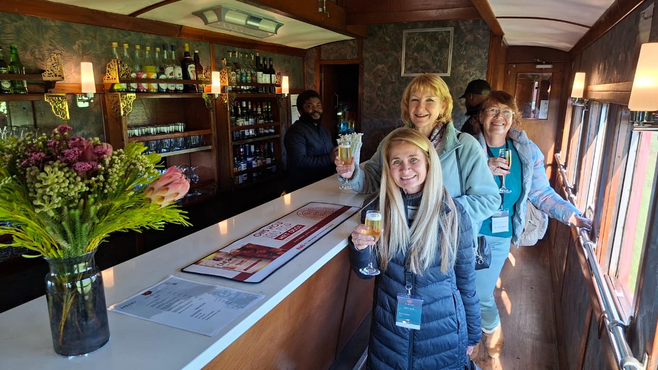 Three women holding drinks inside a train bar.