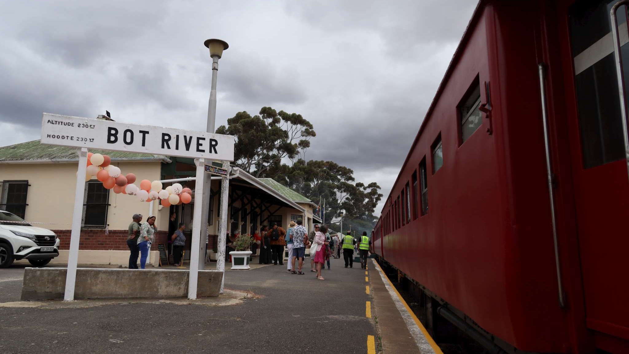People at Bot River station next to a red train.