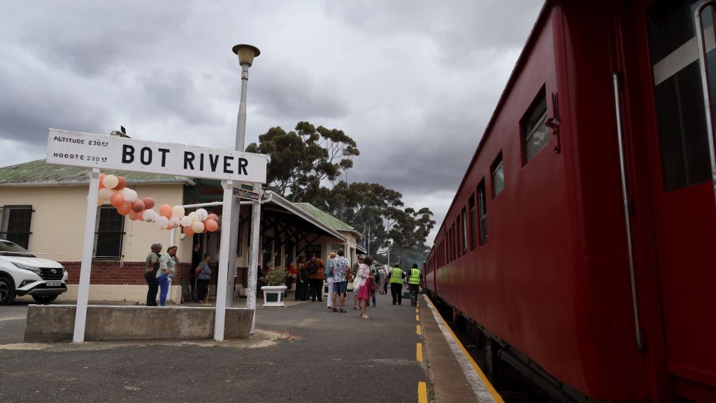 People at Bot River station next to a red train.