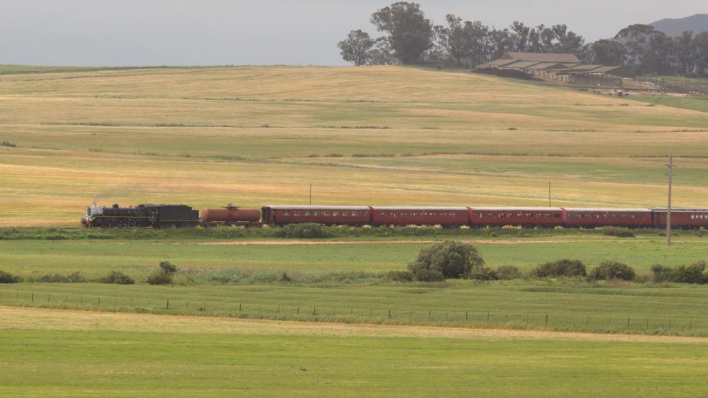 A vintage steam train travels through open grassy fields.