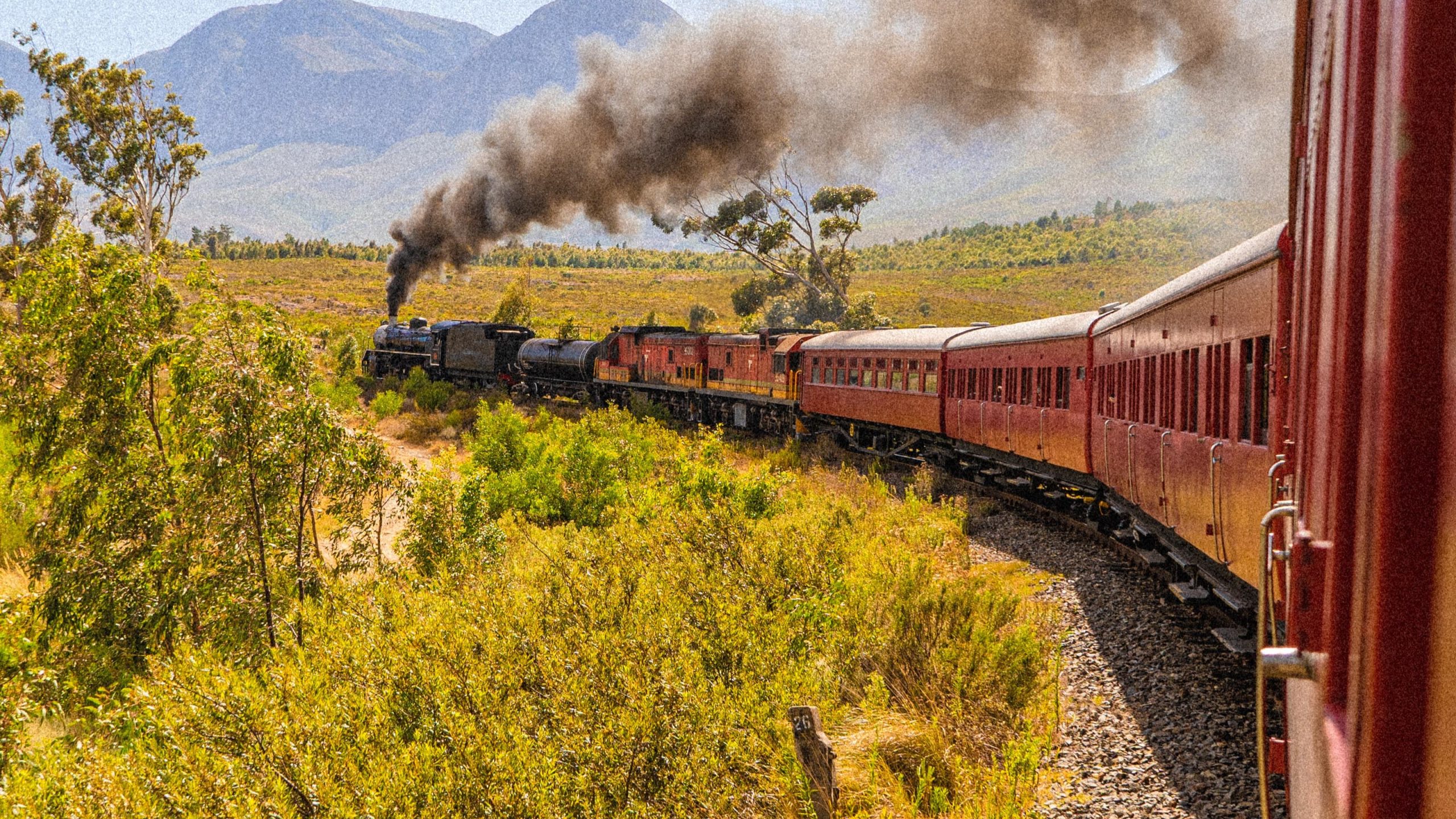 Steam train traveling through a scenic landscape with mountains.