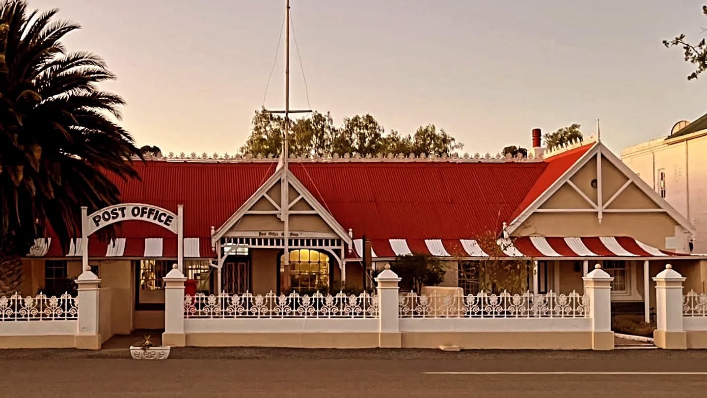 Vintage post office with red roof and striped awnings, surrounded by a white fence.