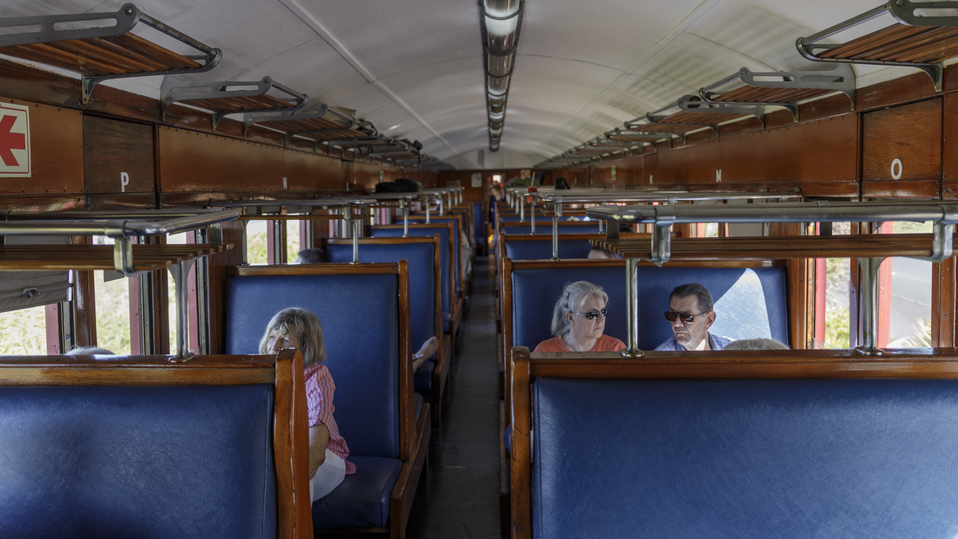 Three passengers seated in a vintage train carriage with blue seats.