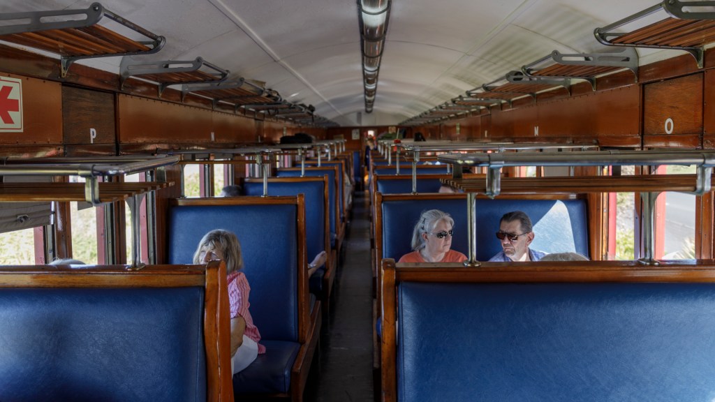 Three passengers seated in a vintage train carriage with blue seats.
