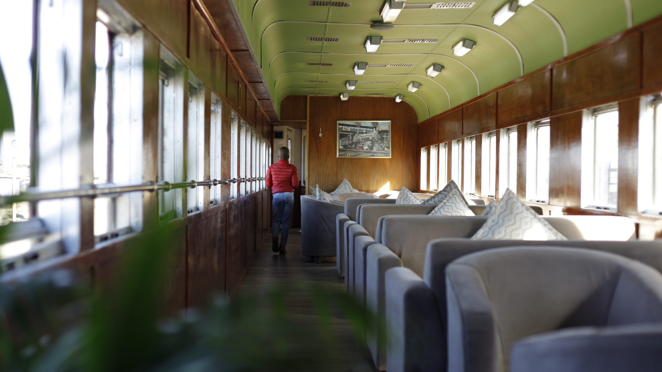 Person walking in a vintage train car with wooden walls and cushioned seats.