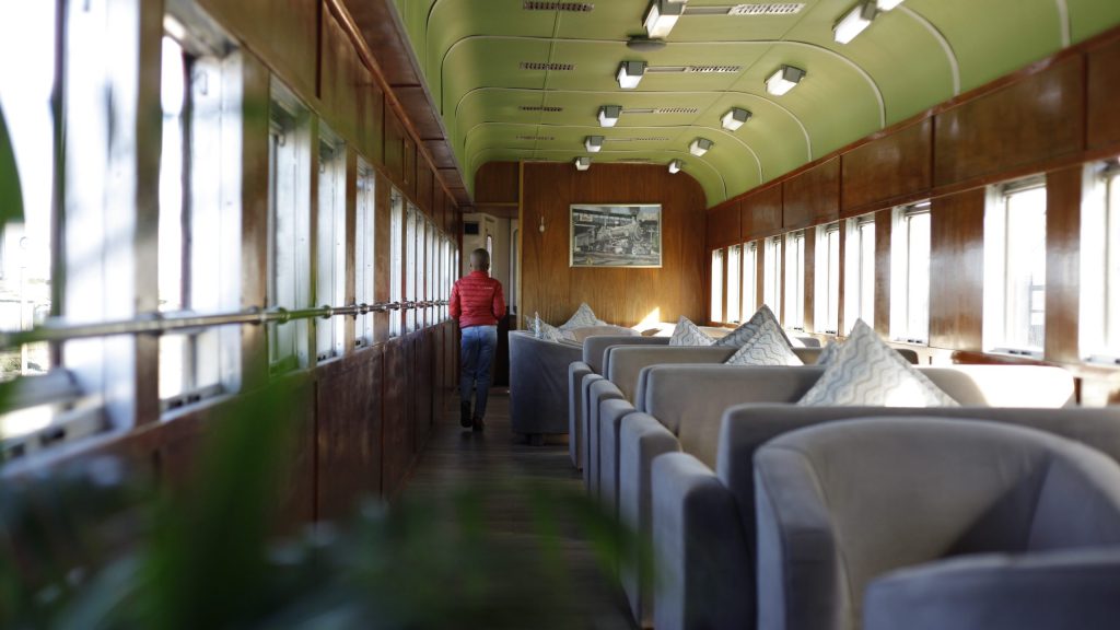 Person walking in a vintage train car with wooden walls and cushioned seats.
