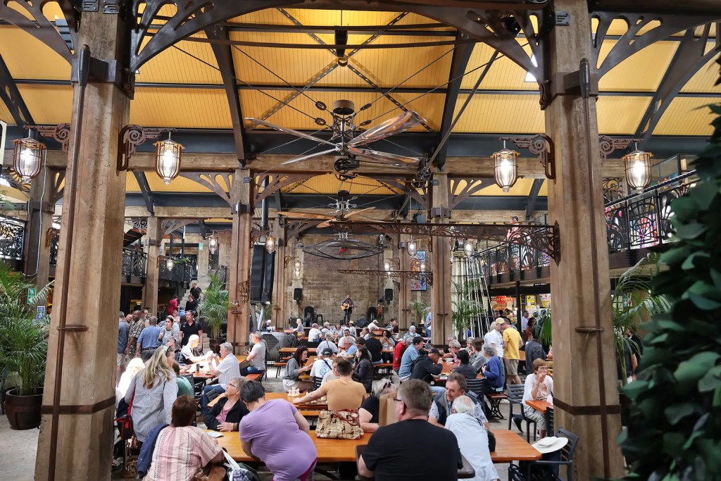 Indoor market with people sitting at tables under high ceiling.