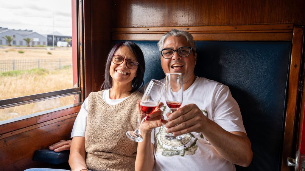 Two people smiling and holding wine glasses in a train cabin.