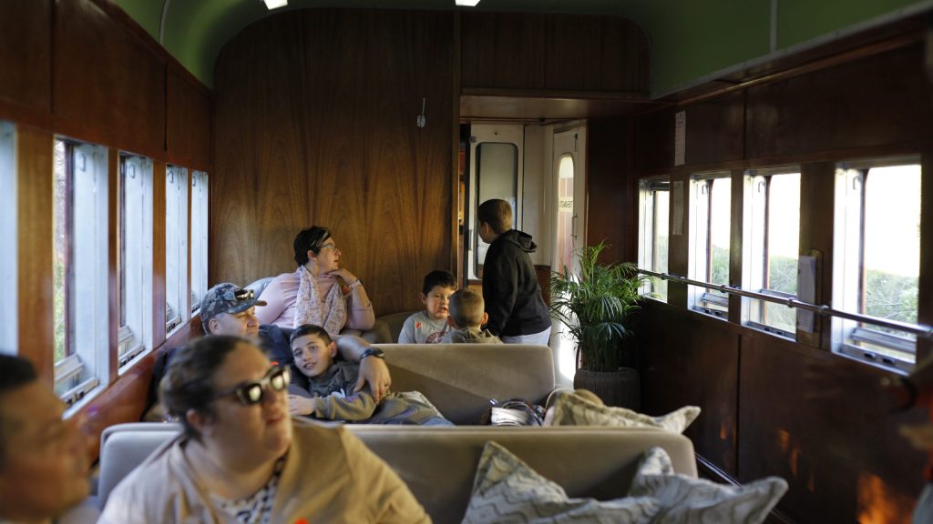 People sitting in a vintage train car with wood paneling.