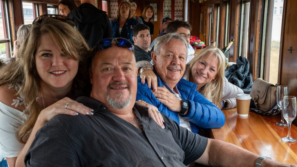 Four smiling people inside a wooden train carriage.