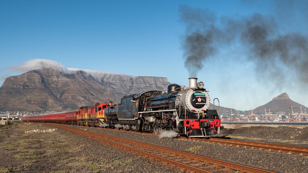 Steam train on tracks with mountains in the background.