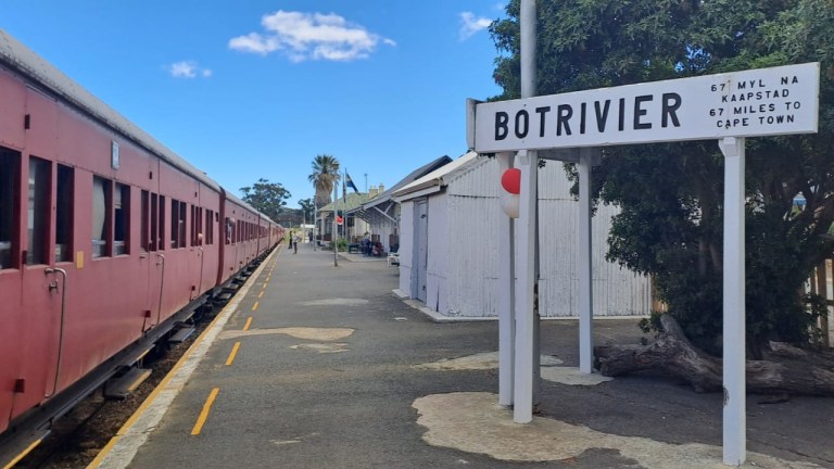 Red train at Botrivier station with sign to Cape Town.