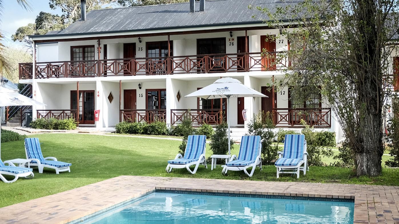 Two-story building with balconies, pool, and lawn chairs in front.
