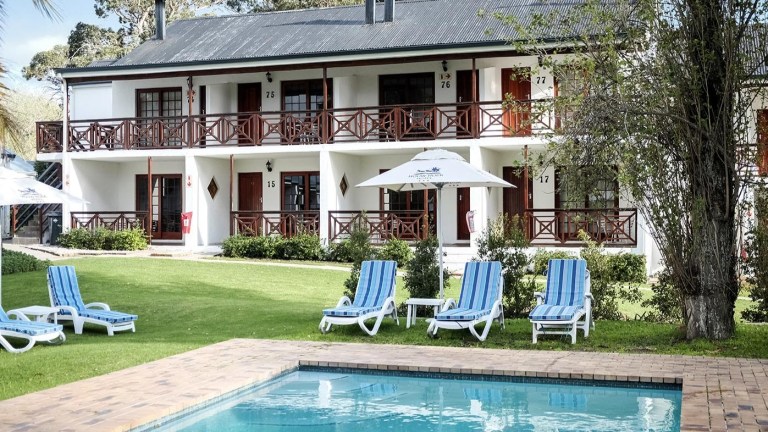 Two-story building with balconies, pool, and lawn chairs in front.