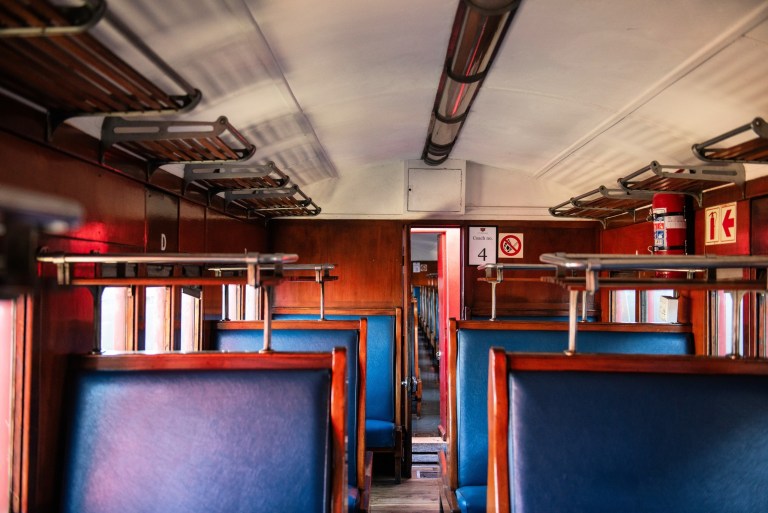 Interior of an empty vintage train car with blue seats and wooden paneling.