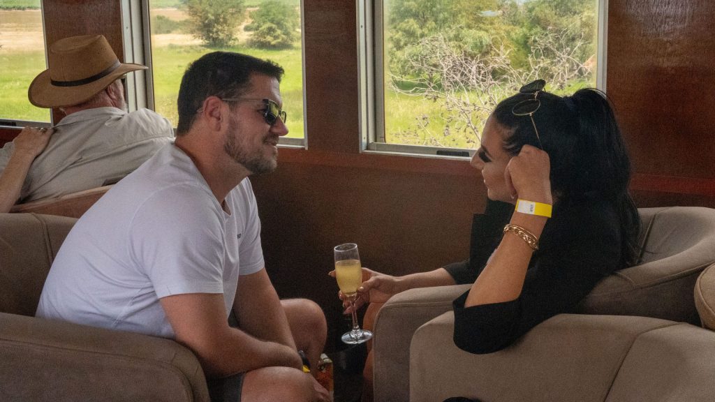 Two people smiling and talking while holding drinks in a train carriage.