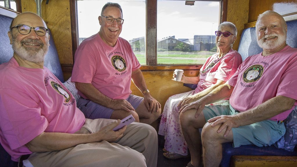 Four smiling seniors in matching pink shirts sitting inside a train.