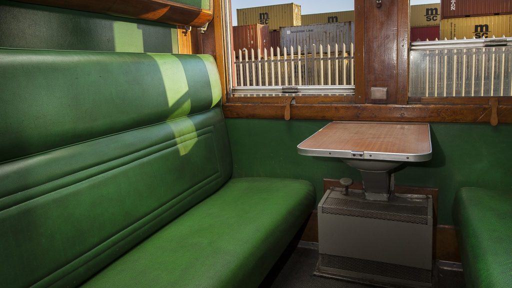 Vintage train compartment with green seats and a wooden table.