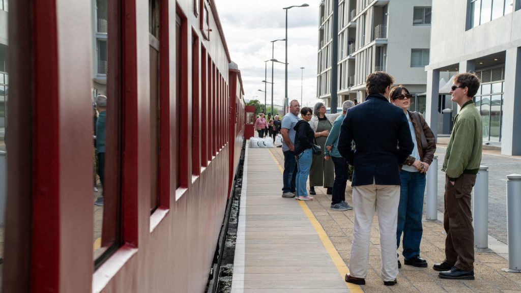 People standing on train platform beside a red train.