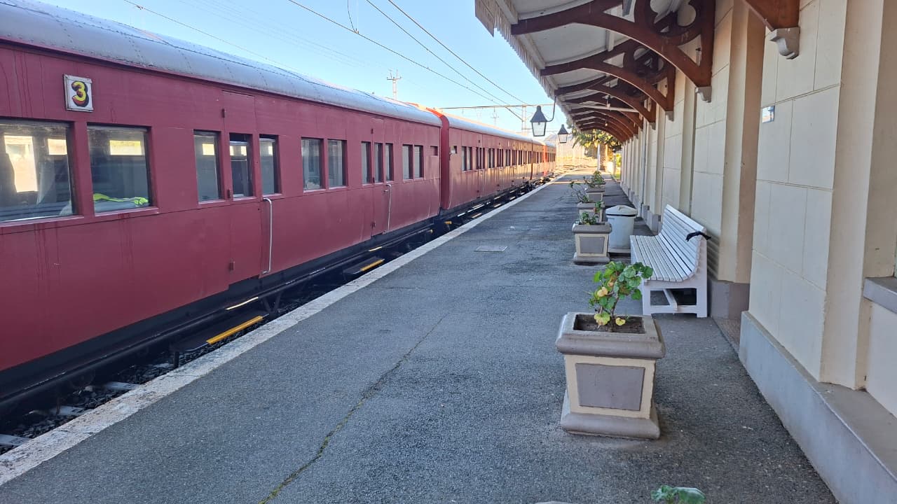 Vintage red train at a quiet station platform with benches and potted plants.