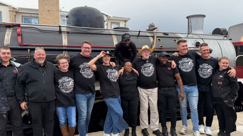 Group of people in black shirts pose in front of a vintage steam train.