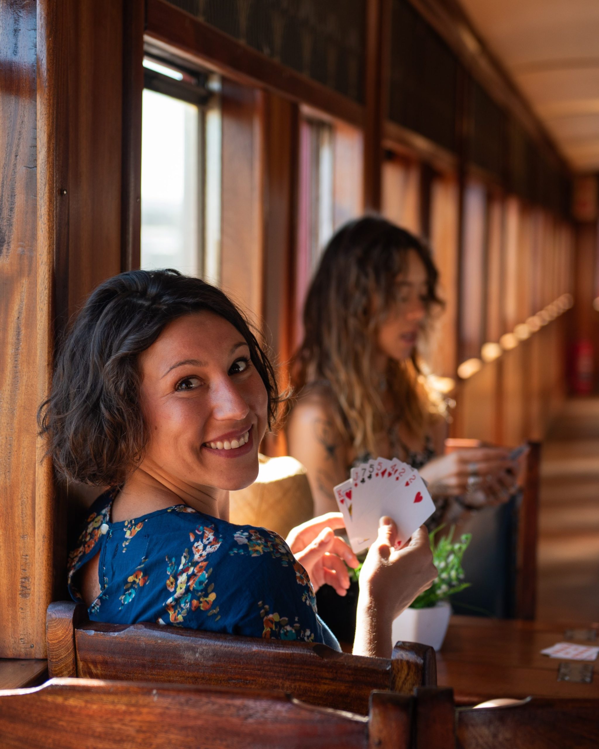 Woman on train holding cards, smiling at camera, another woman in background.