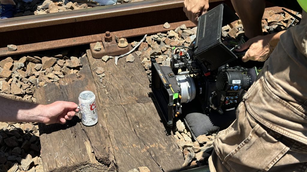Camera filming a hand placing a can on railway tracks.