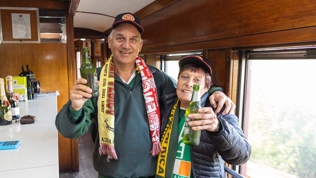 Two people in sports scarves holding beer bottles on a train.