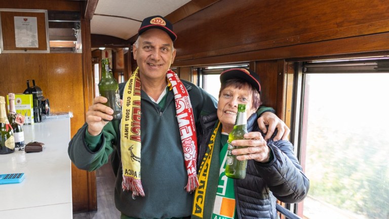 Two people in sports scarves holding beer bottles on a train.