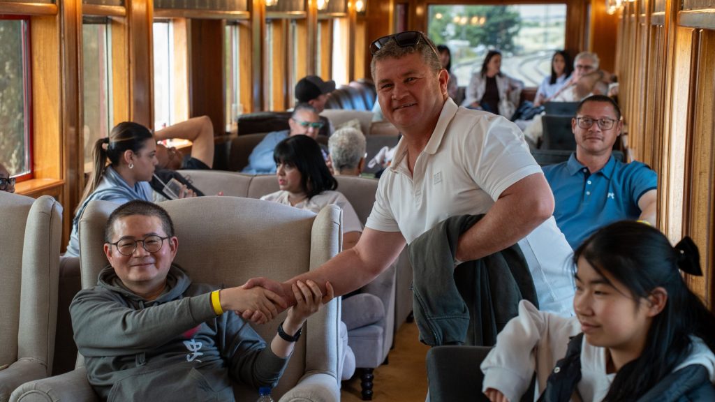 People sitting in a train carriage, two men smiling and shaking hands.