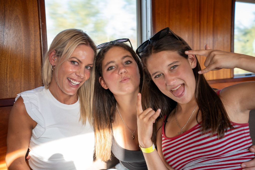 Three women smiling and posing on a train, with wooden interior.