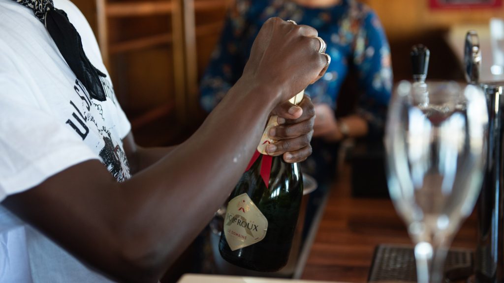 Person opening a champagne bottle behind a bar.
