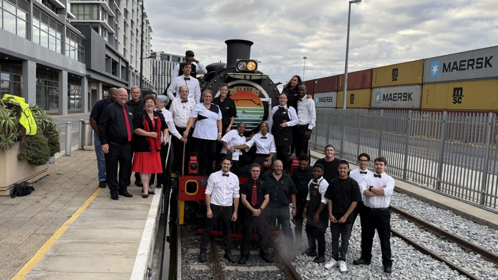 Group of people pose on and around a stationary train at a railway platform.
