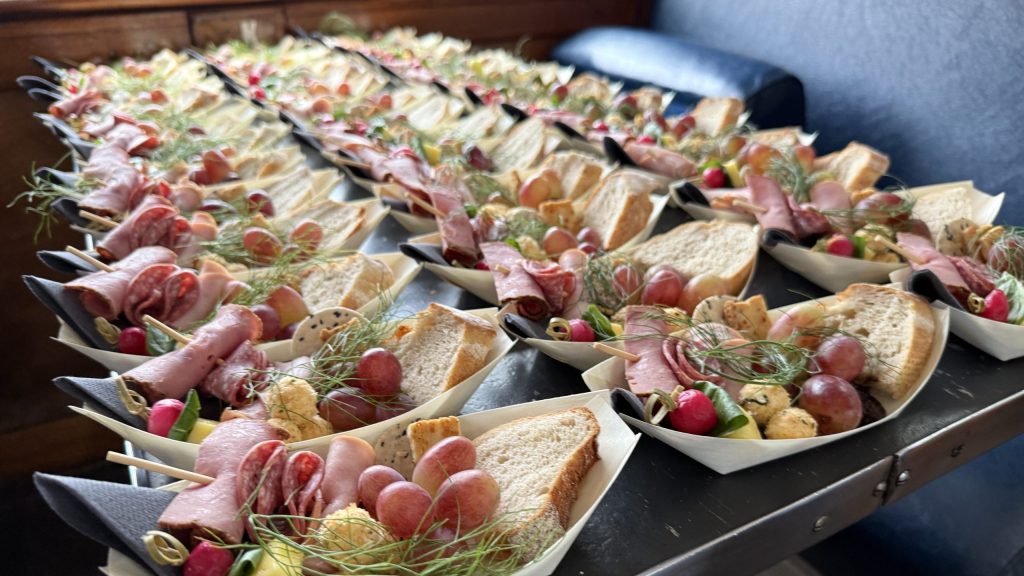 Multiple plates with meats, bread, grapes, and garnish arranged on a table.