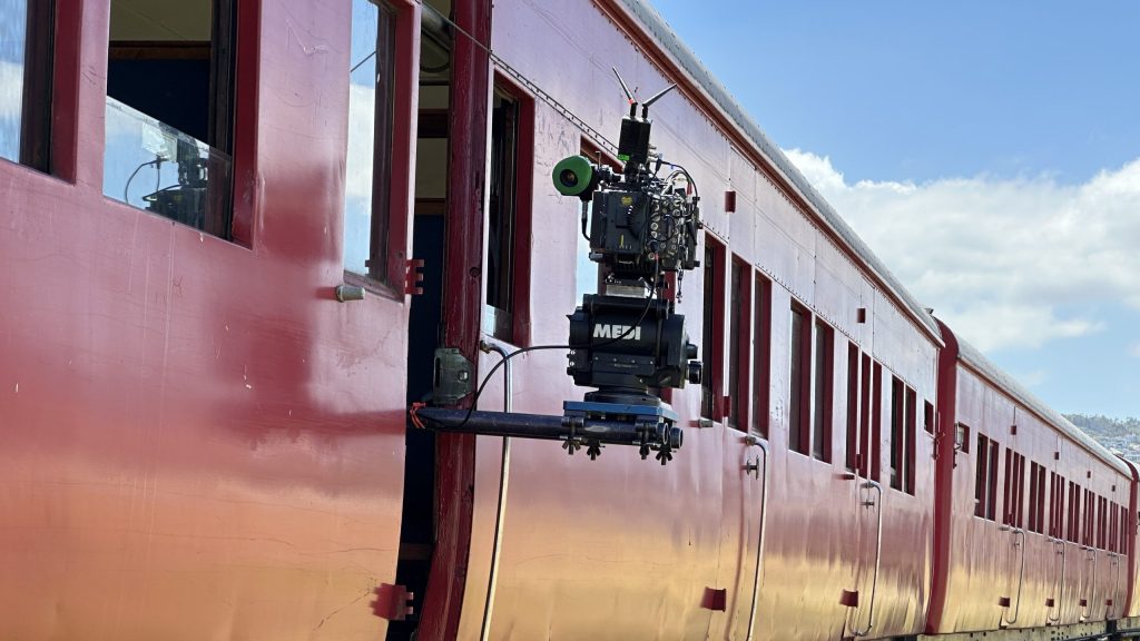 Film camera mounted on side of moving red train.