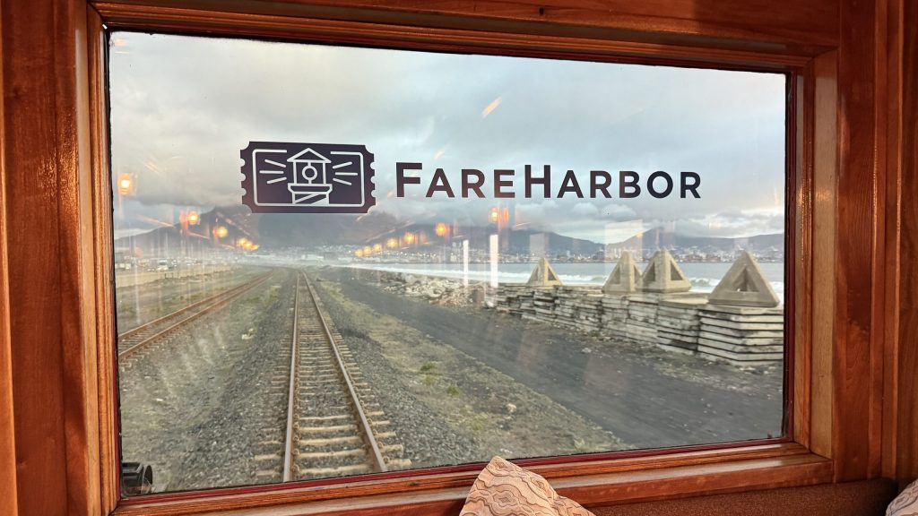 View of train tracks and mountains through a window labeled 'FareHarbor.'
