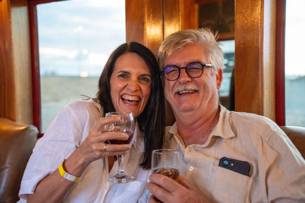 Smiling couple sitting with drinks, man wearing glasses and white shirt.