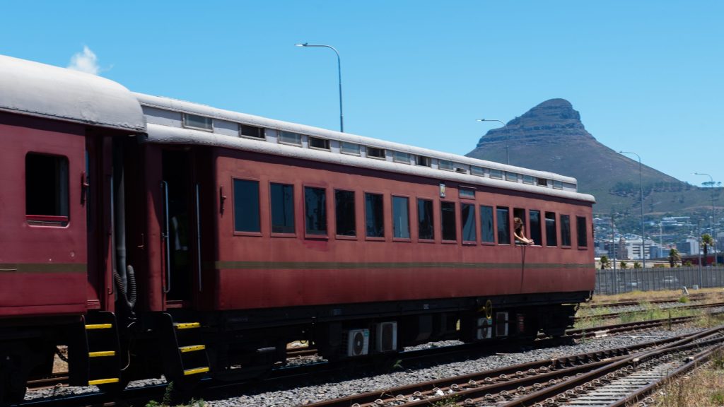 Red train on tracks with mountain and clear blue sky in background.