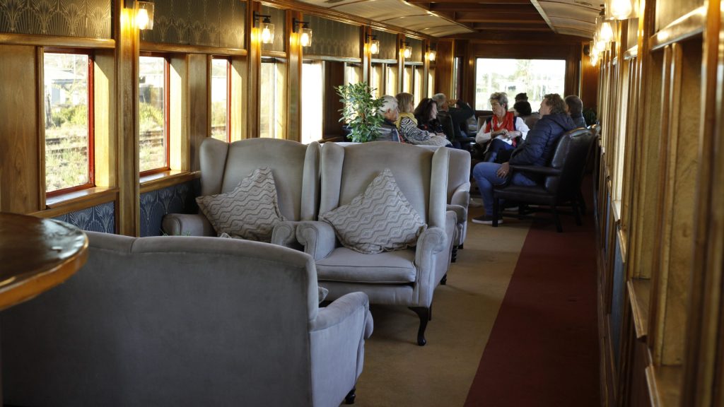 Passengers seated in a cozy train car with armchairs and large windows.