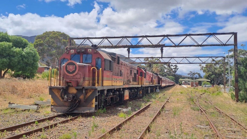 Old freight train on tracks under a cloudy sky with trees around.