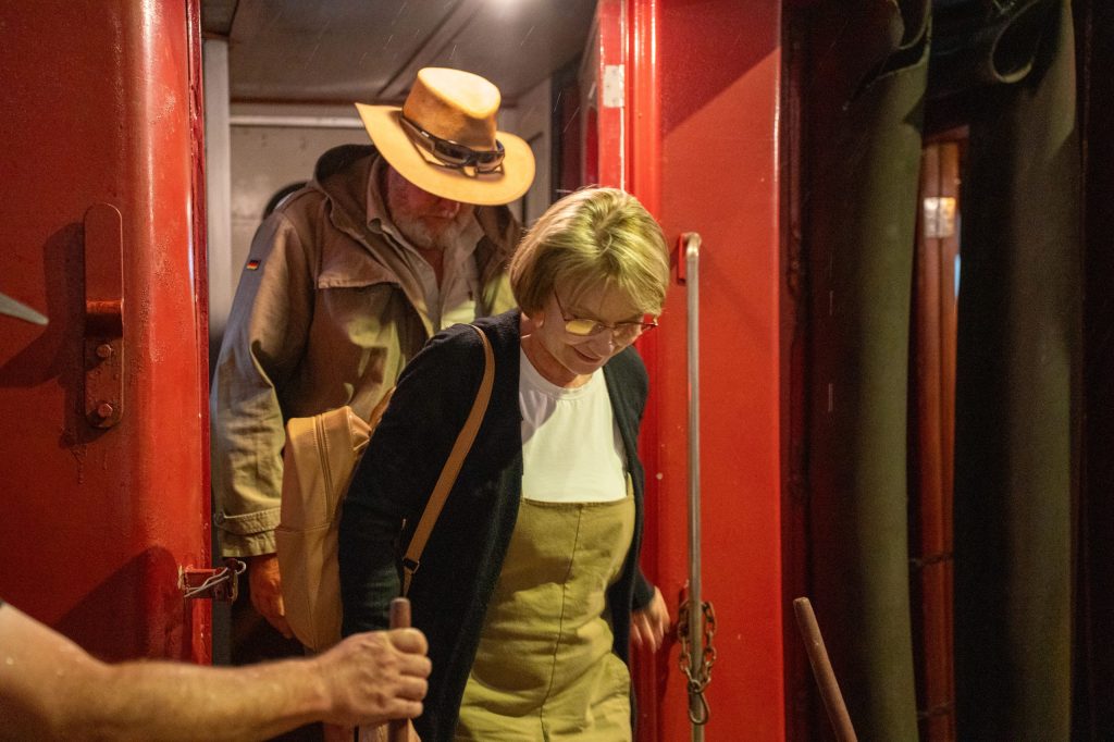 Two people exiting a red train car, wearing casual hats and jackets.