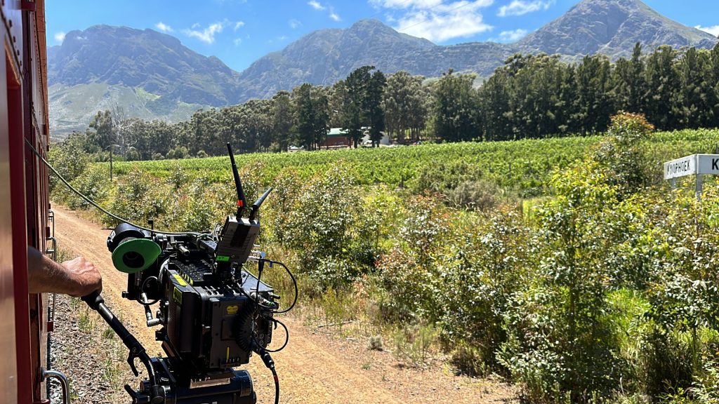 Camera on train filming scenic landscape with mountains and greenery.