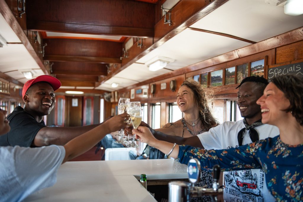 Group of people toasting with drinks inside a train dining car.