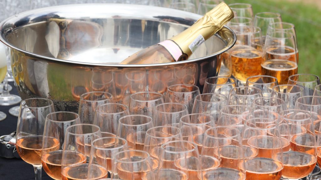Champagne bottle in ice bucket with many filled glasses nearby.
