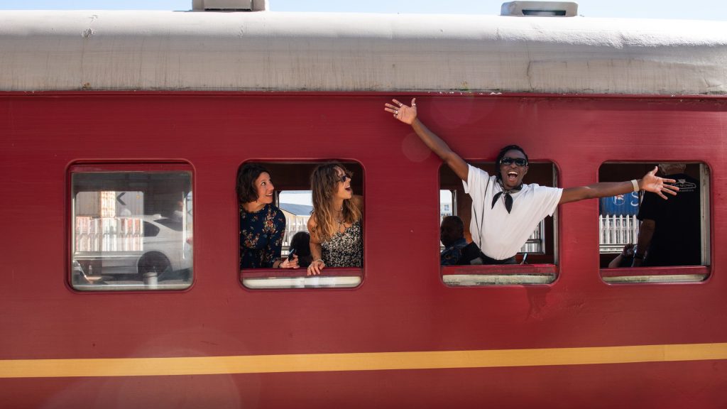 Group of people smiling and waving from a red train window.
