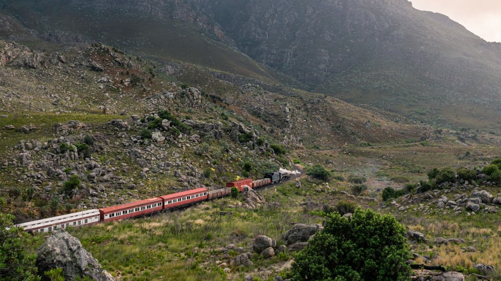 Train traveling through a rocky mountain landscape with green vegetation.