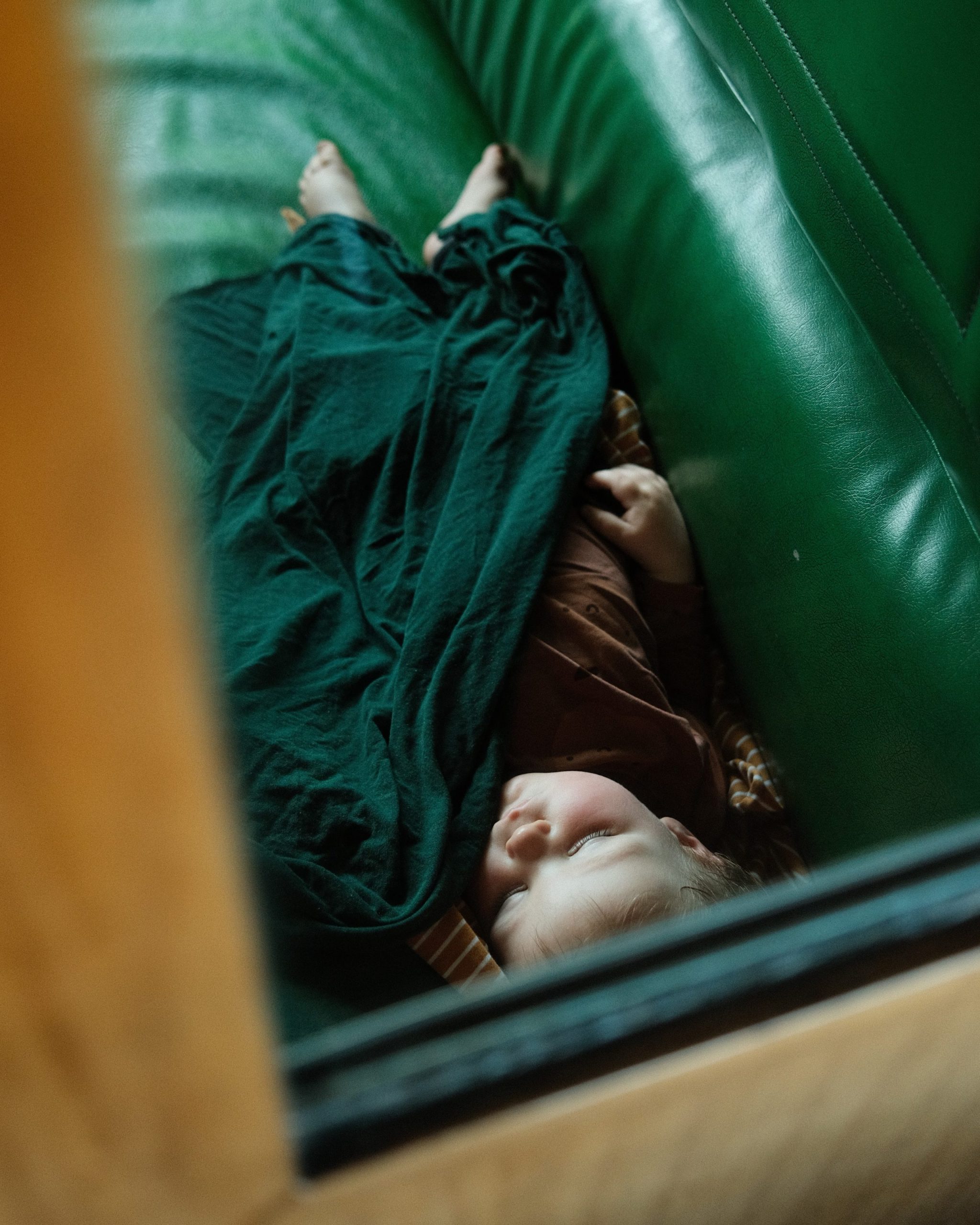 Child sleeping on a green couch with a green blanket.