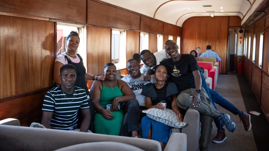 Group of people smiling inside a train with wooden interior.