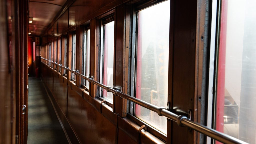 Narrow train corridor with wooden walls and windows on one side.