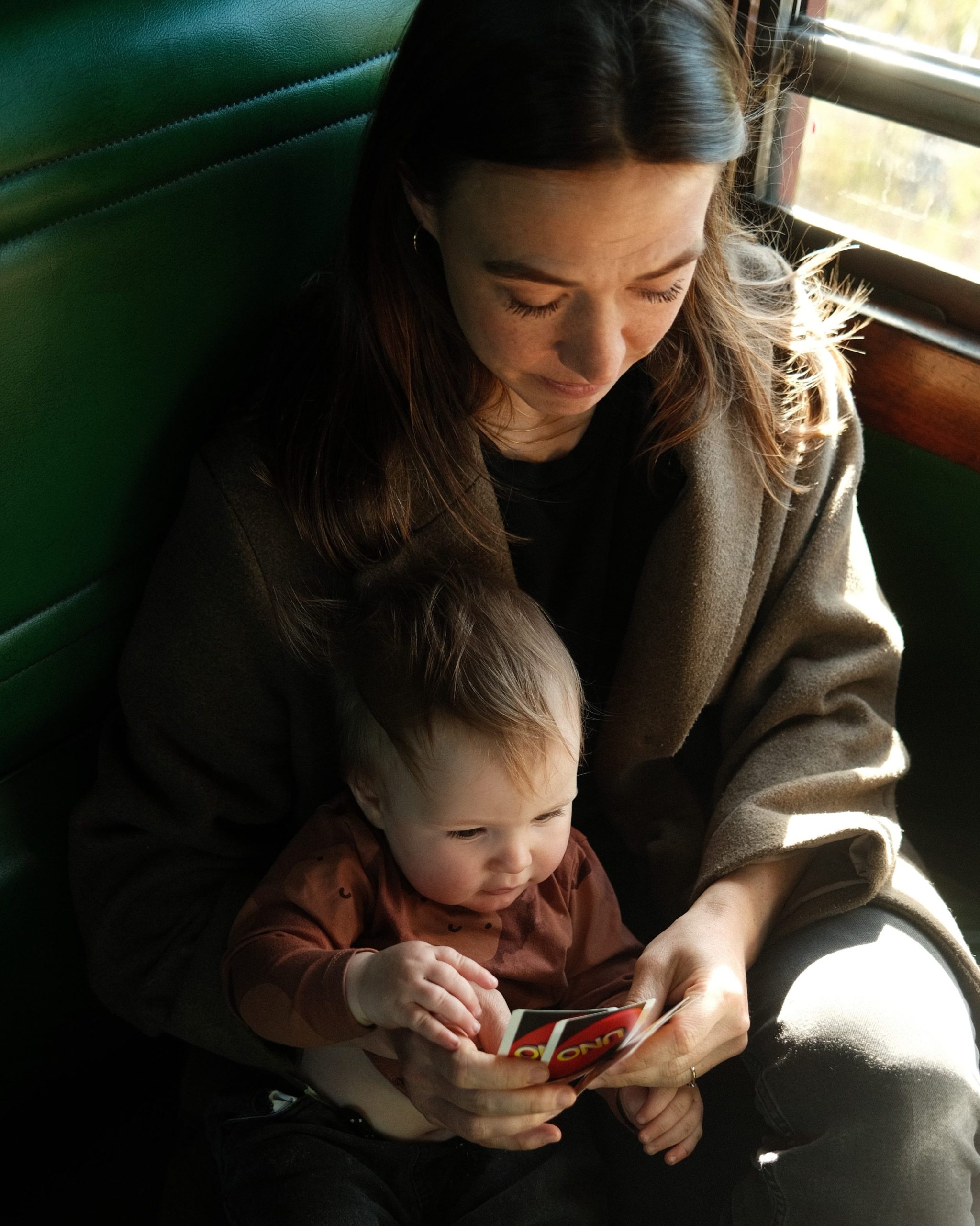 Woman holding a baby on a train seat, both looking at a small book.